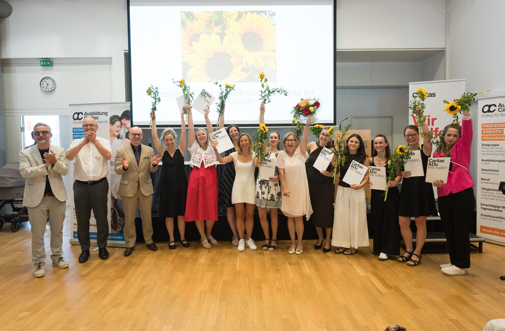 Absolventinnen mit Blumen und Zeugnissen bei Caritas-Veranstaltung in Österreich