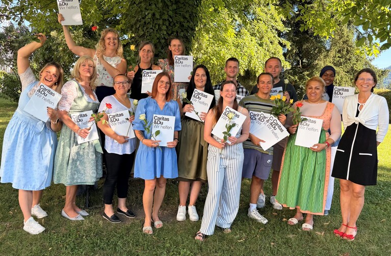 Caritas-Mitarbeiterinnen und -Mitarbeiter mit Blumen und Zertifikaten im Freien