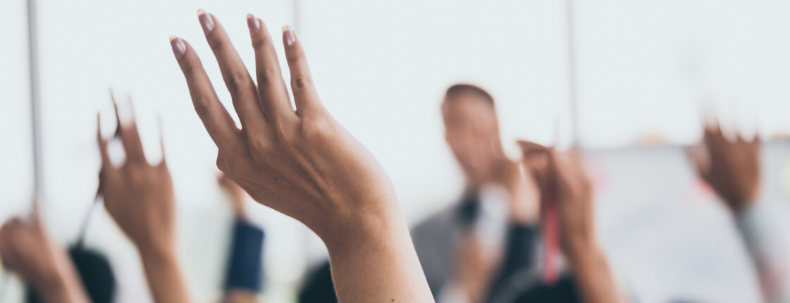 Audience raising hands up while businessman is speaking in training at the office.